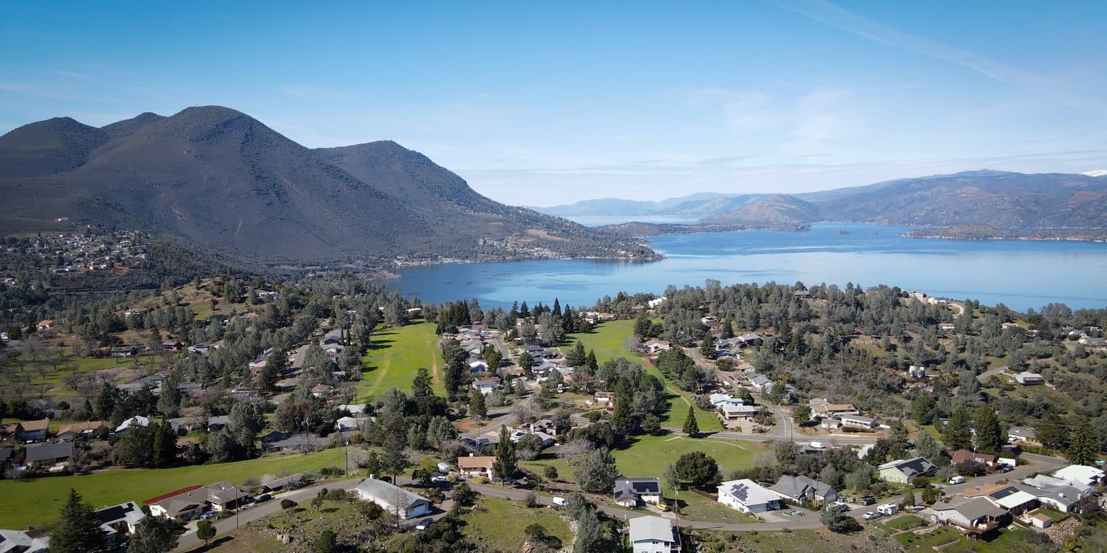 A lakeside community spread across the slope below forested mountains.